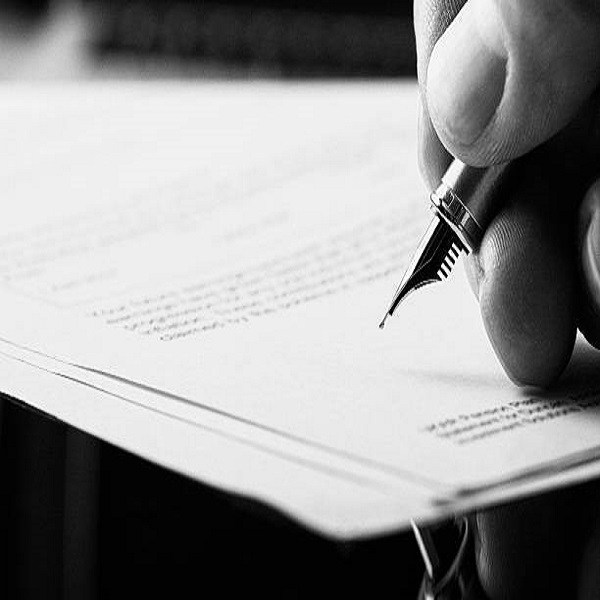 A hand holding a fountain pen and about to sign a letter. Styling and small amount of grain applied.